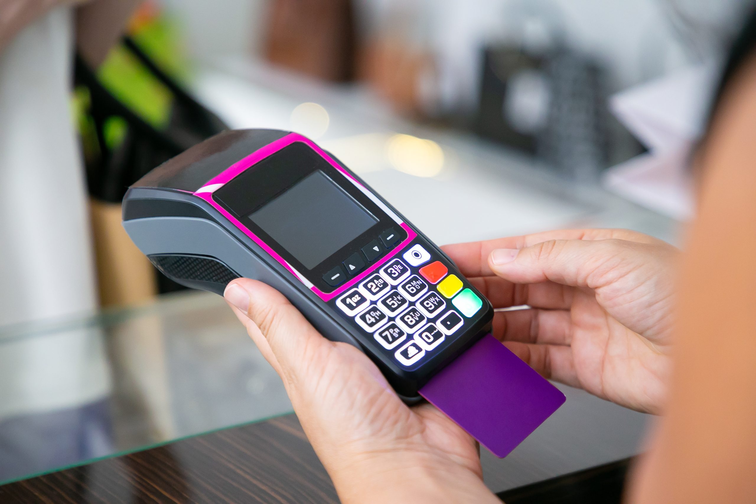Pessoa segurando uma máquina de cartão moderna, com cartão roxo inserido, pronta para realizar uma transação eletrônica em um ambiente comercial.