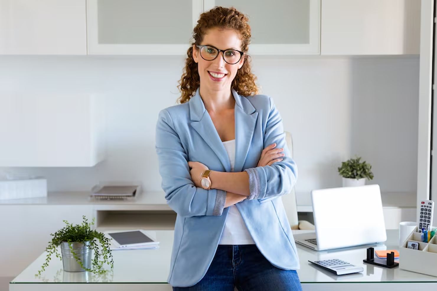 Mulher confiante de pé em frente a uma mesa de escritório moderna, com expressão positiva e braços cruzados, simbolizando segurança e tomada de decisão — uma representação visual de empoderamento financeiro no ambiente profissional.