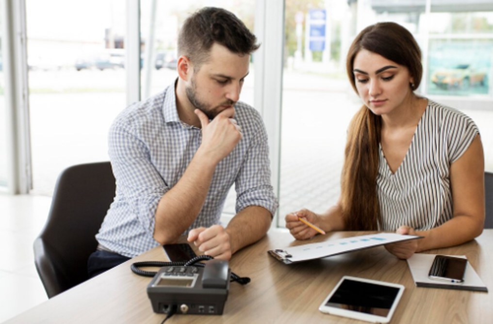Homem e mulher analisando gráficos e documentos em um escritório moderno, discutindo condições de empréstimo pessoal e avaliando propostas financeiras antes da contratação.