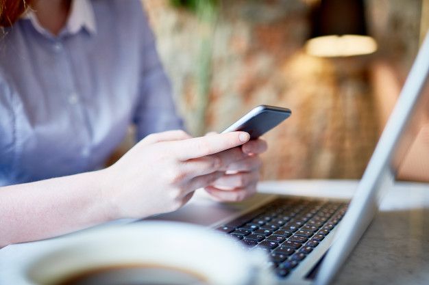 Pessoa utilizando o celular enquanto trabalha em frente ao notebook, simbolizando a praticidade de solicitar um empréstimo pessoal de forma online e rápida.