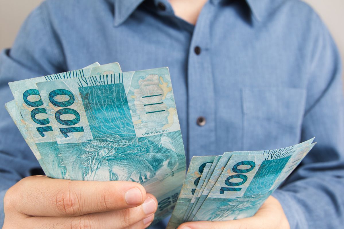 Pessoa segurando várias cédulas de 100 reais, representando o acesso rápido a dinheiro por meio de crédito pessoal.