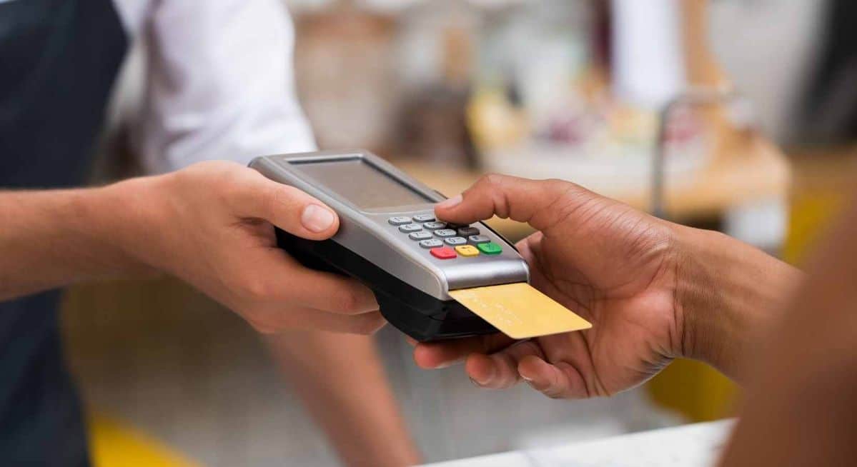 Cliente realizando pagamento com cartão em uma maquininha de cartão no balcão de atendimento.